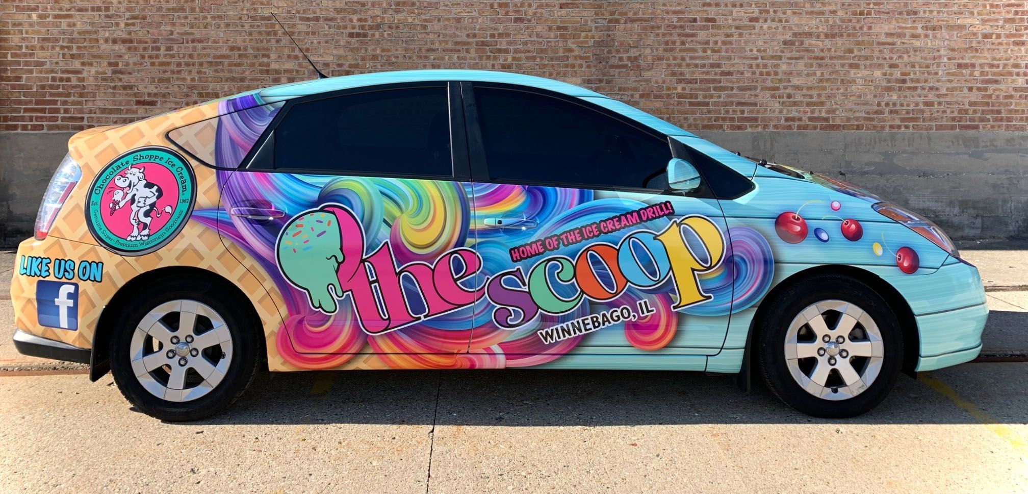 A small car that has been colorfully wrapped with graphics promoting an ice cream business called "The Scoop"
