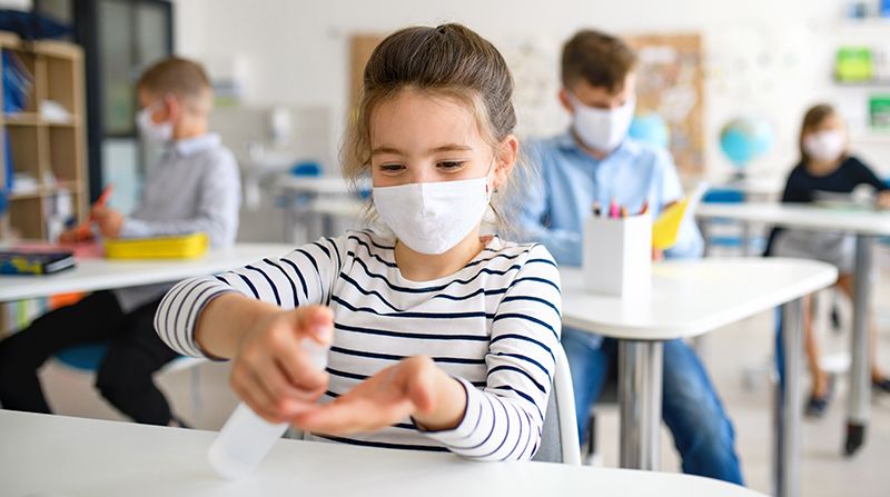 Young girl using hand sanitizer at school